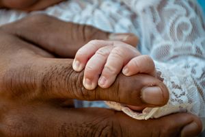 Close-up view of tiny newborn hands against a white lace background.