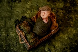 A sleeping baby nestled in a rustic wooden box surrounded by natural foliage.