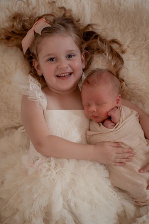 Sweet portrait of siblings in cream-colored dresses laying together.