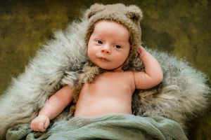 Baby lying on soft grey fur blanket wearing fuzzy animal ear hat in studio portraits.