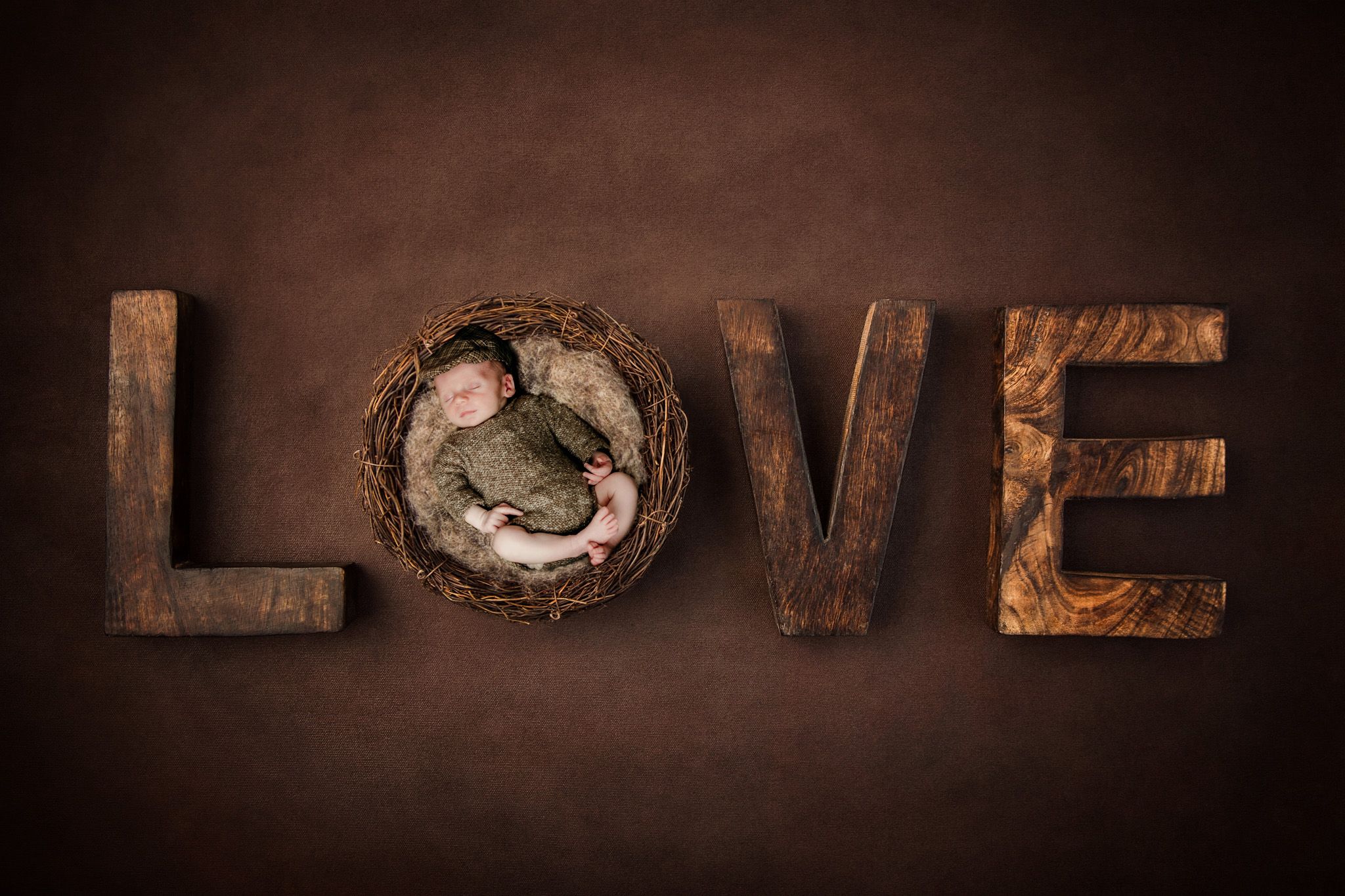 Creative newborn photography with baby in nest forming letter O in wooden LOVE text.