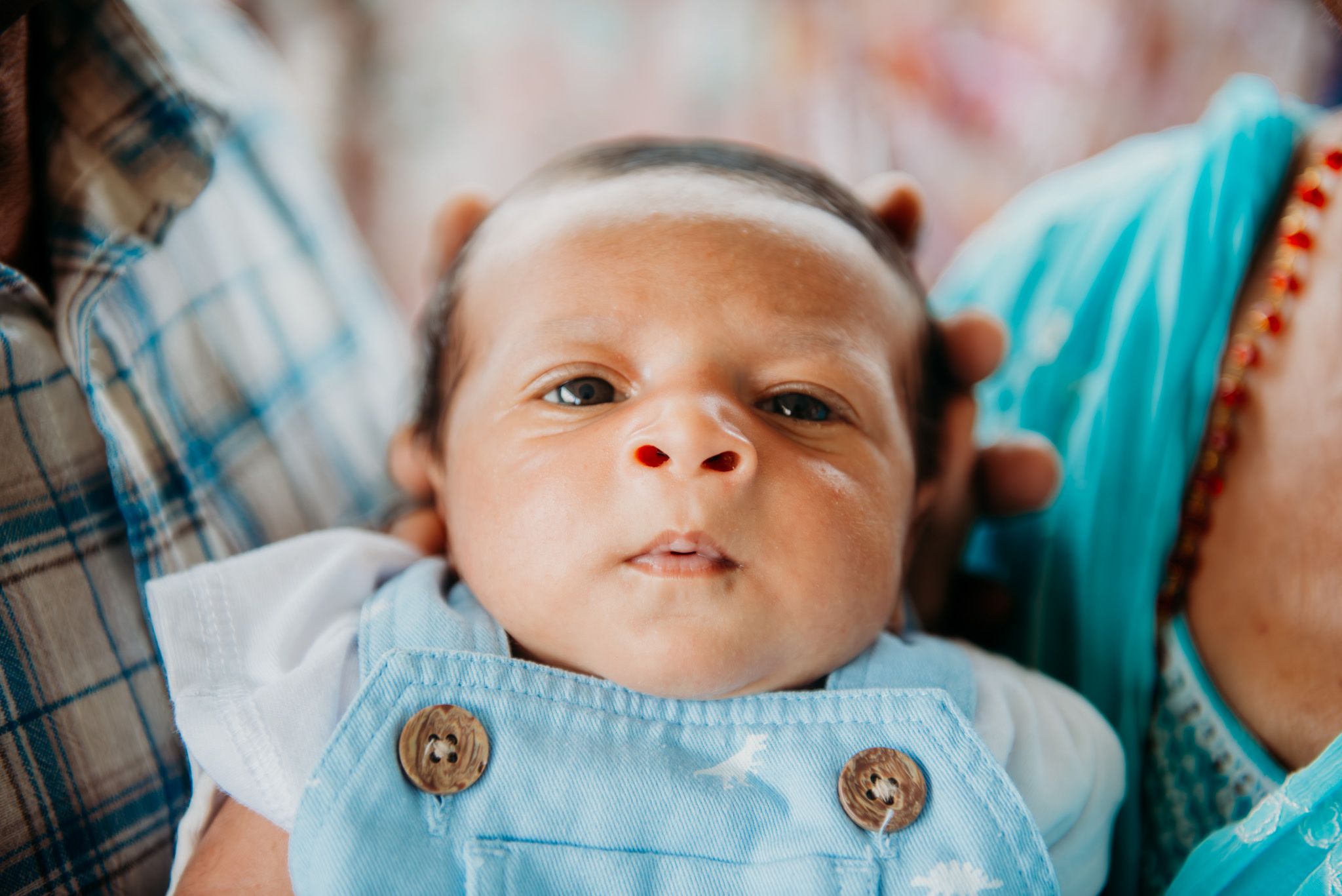 Infant wearing light blue overalls with decorative buttons.