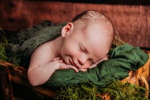 Sleeping newborn on green moss with rustic wood background.