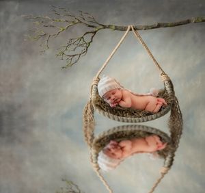 Rustic wooden branch swing with cozy knitted hammock against grey backdrop.