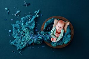 Artistic water-themed newborn photography setup with blue tones and wooden props.