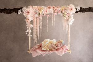 Floral swing decoration with pink flowers and hanging crystals against gray backdrop.