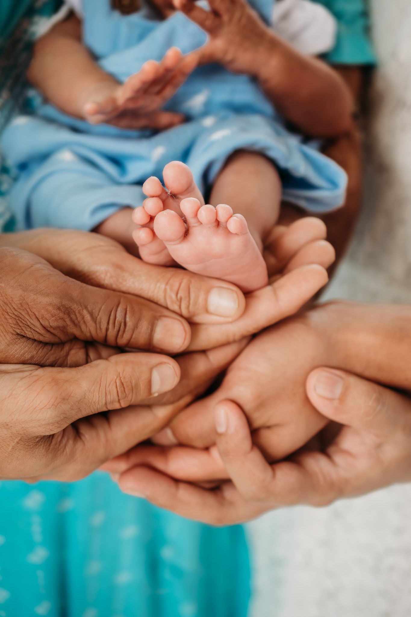Gentle hands tenderly holding tiny baby feet against a turquoise background.