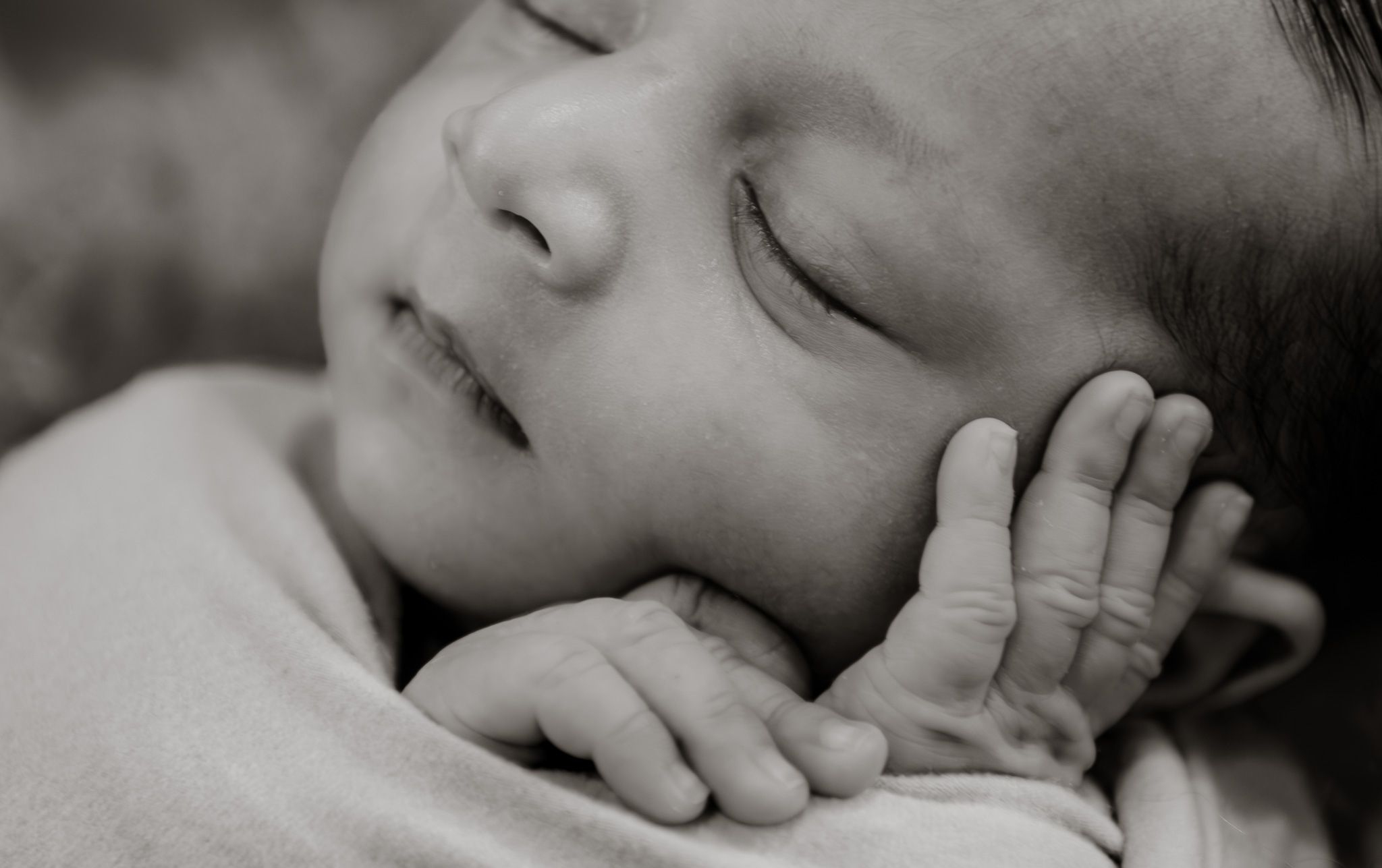 Black and white portrait of sleeping infant with hand near face.