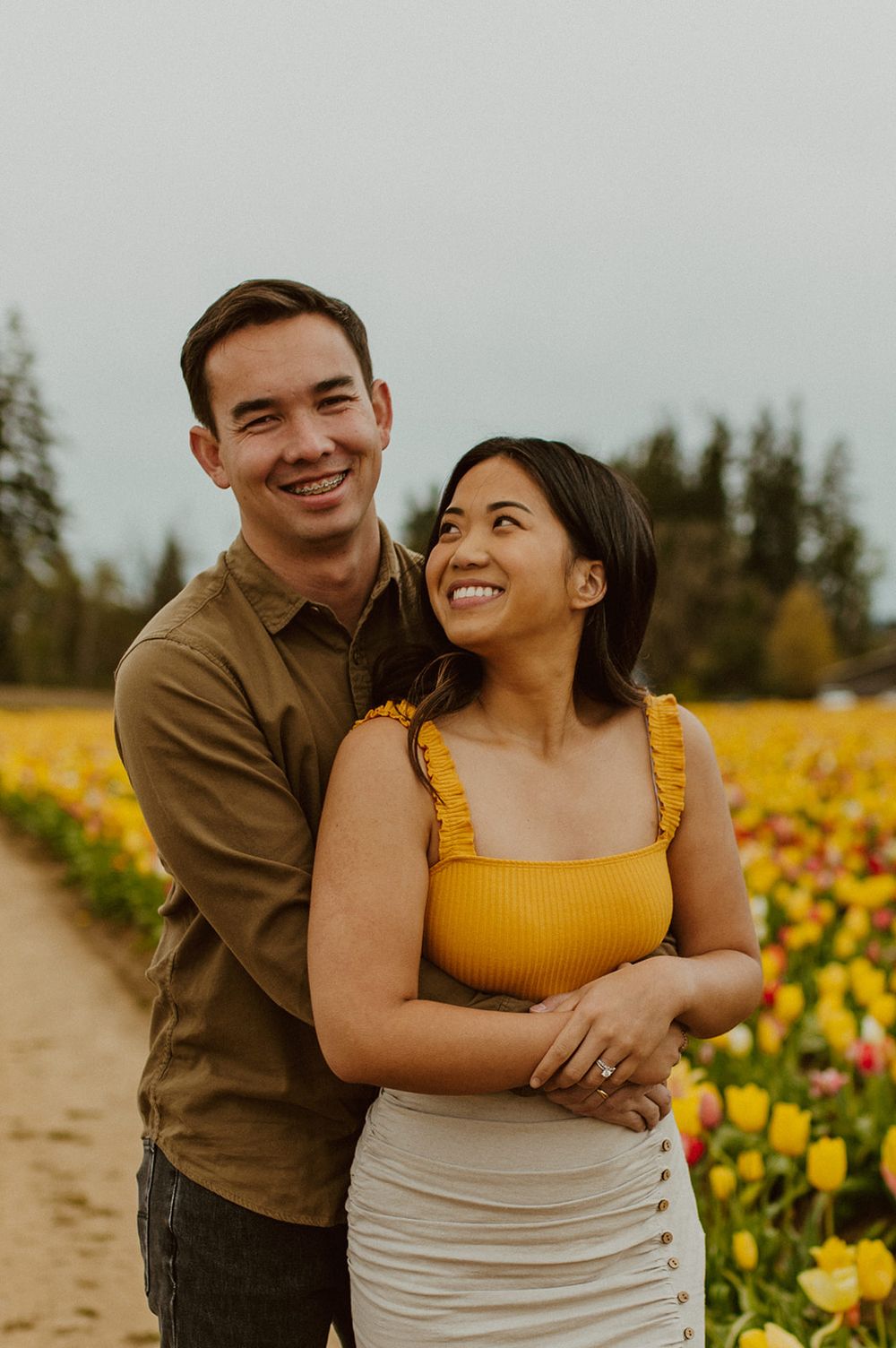 A joyful couple laughs together while standing among colorful tulip fields.