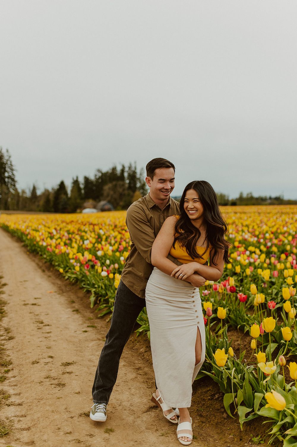 A couple shares a playful moment while walking through rows of vibrant tulips.