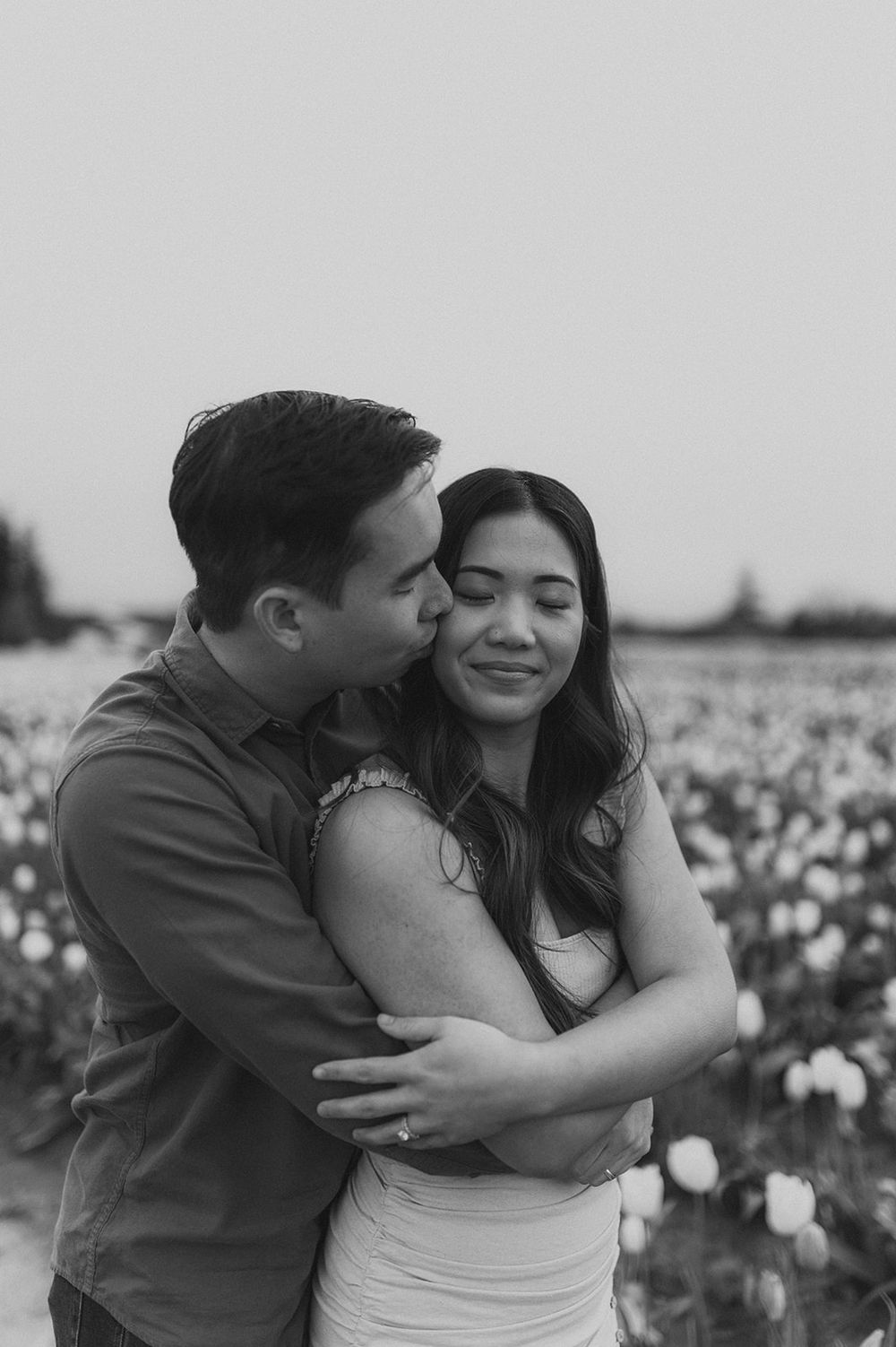 An intimate black and white photo of a couple embracing in a flower field.