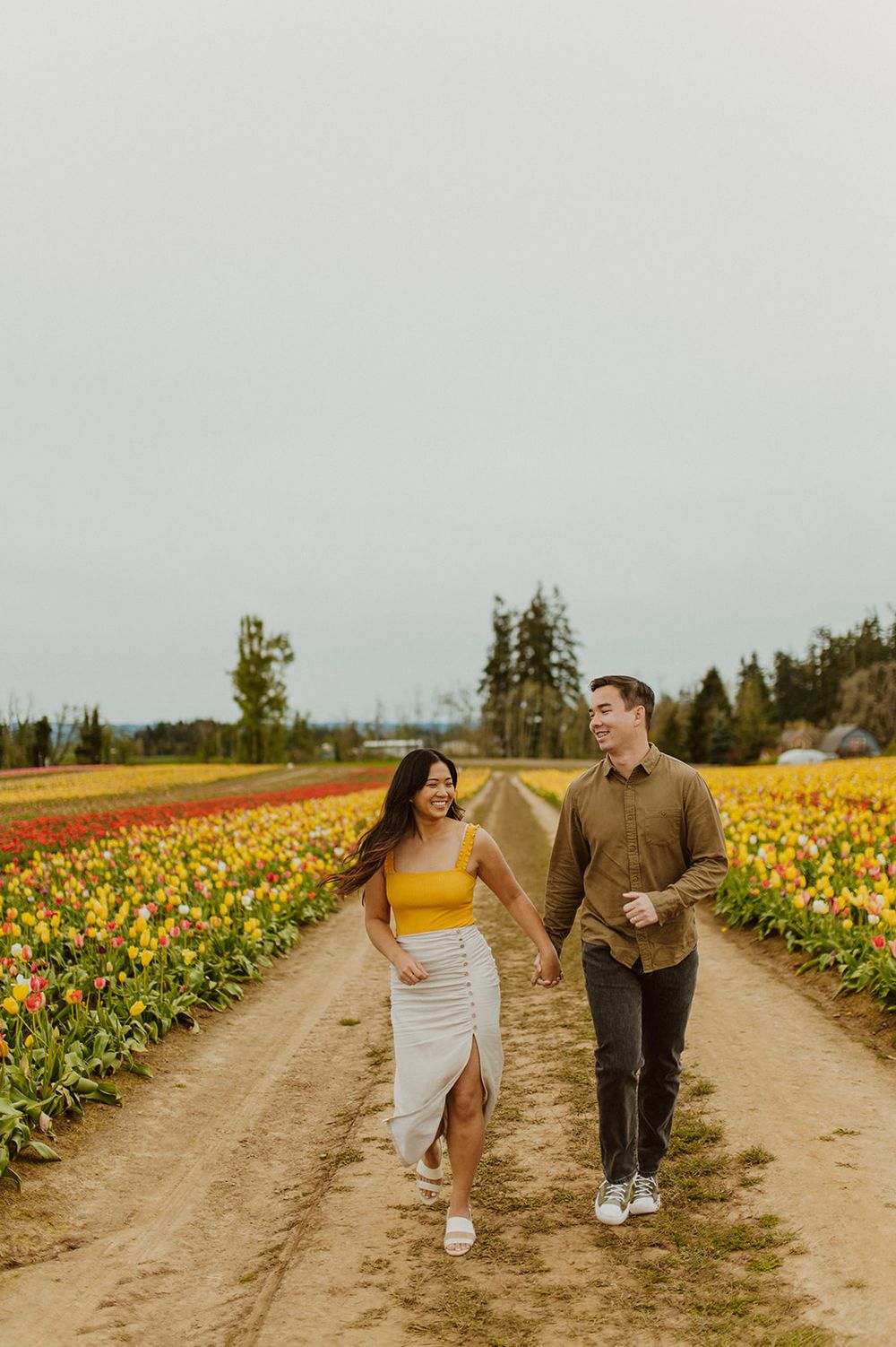 A couple takes a romantic stroll down a dirt path between rows of colorful tulips.