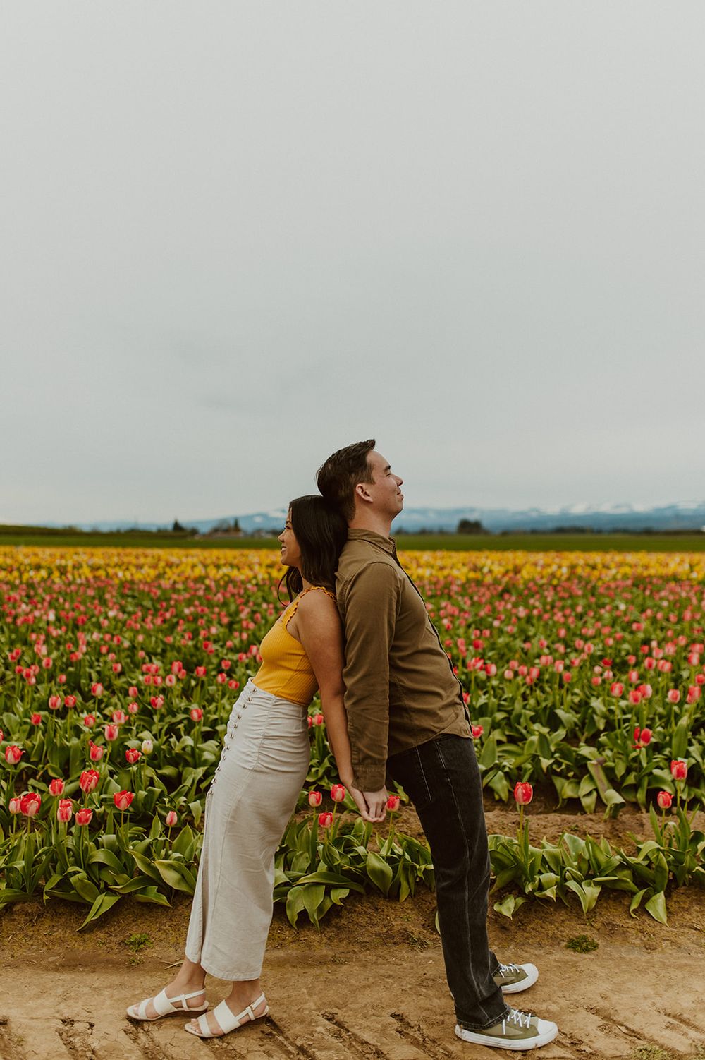 A couple leans back-to-back playfully in a vast field of blooming tulips.