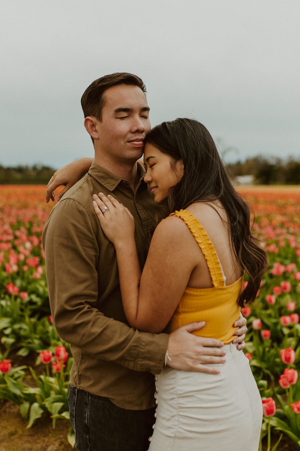 Couple embraces intimately among colorful tulip flowers on an overcast day.