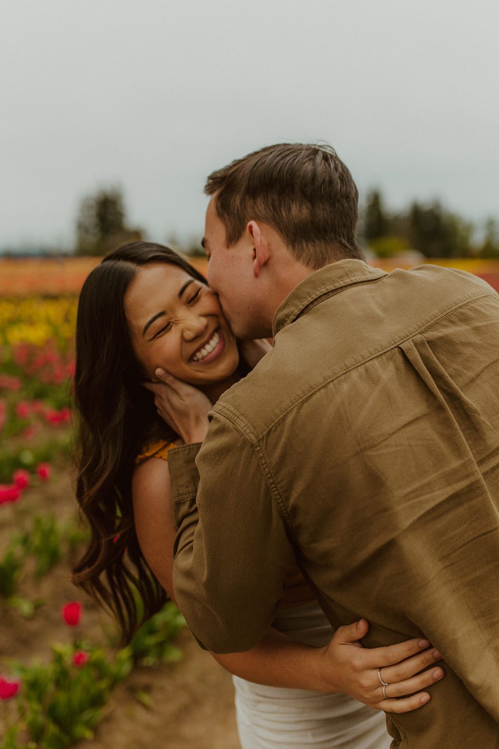 A couple shares laughter and affection while embracing in a field of flowers.
