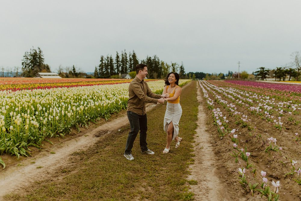 Happy couple dances together on a dirt path between rows of blooming flowers.