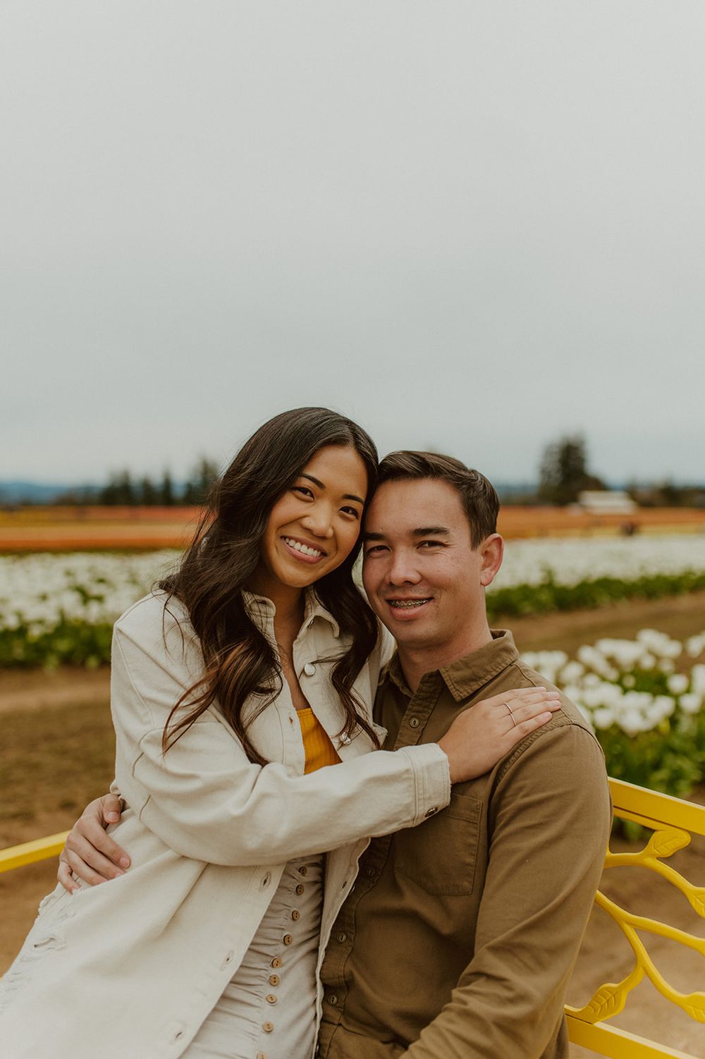 Couple shares a happy moment while sitting on yellow bench in flower field.