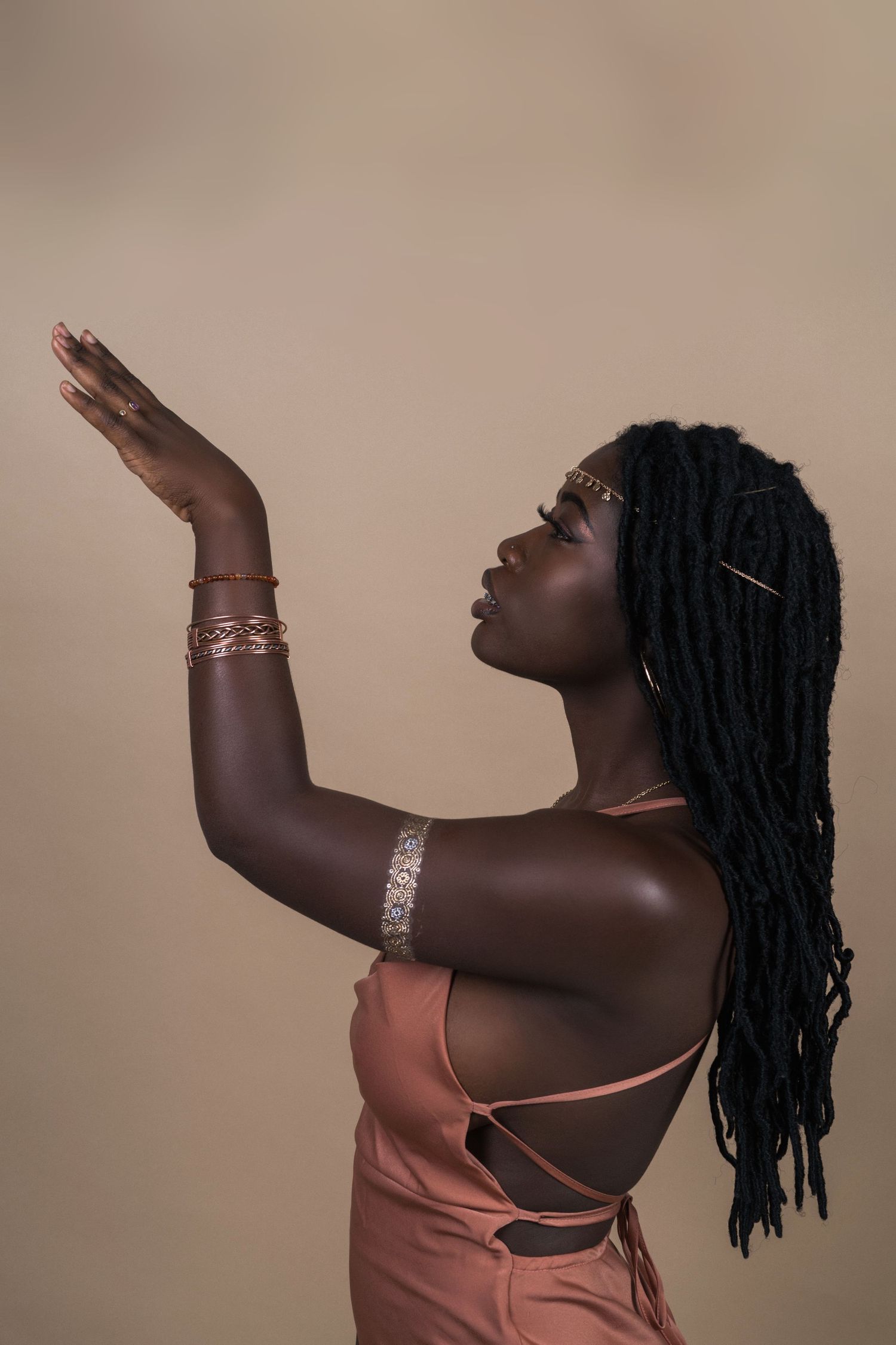 Artistic portrait of someone in coral dress with dreadlocks raising hand gracefully against neutral background.