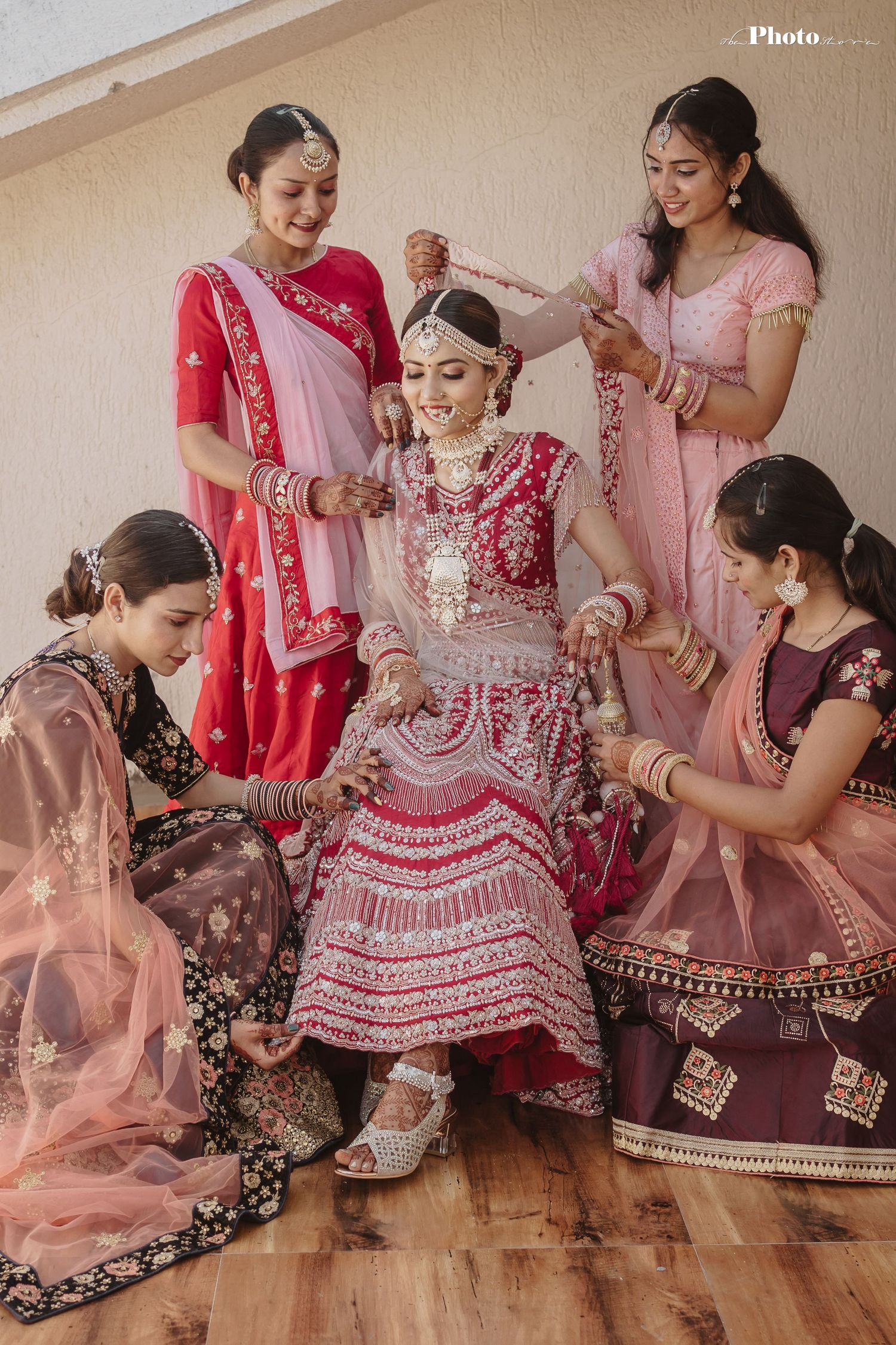 Wedding preparation scene with traditional red and pink lehenga and bridesmaids in coordinated attire.