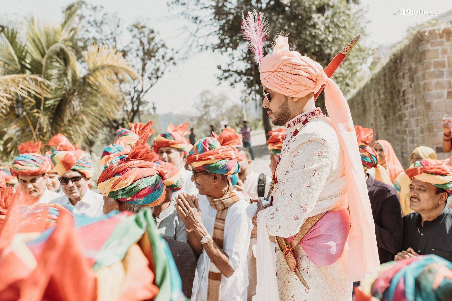 Outdoor wedding celebration with guests wearing orange turbans in natural setting.