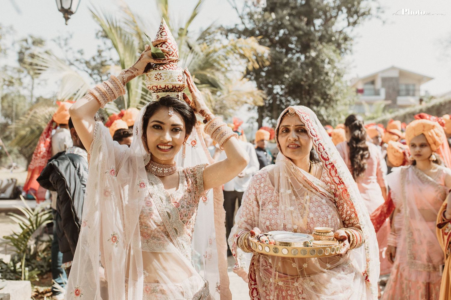 Celebratory crowd in white and coral attire dancing during outdoor Indian wedding festivities.