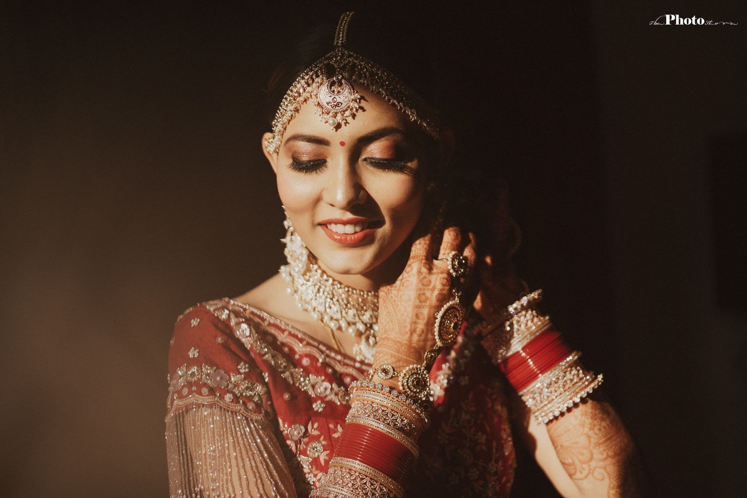 Artistic portrait of Indian bride wearing traditional jewelry and red outfit in moody lighting.