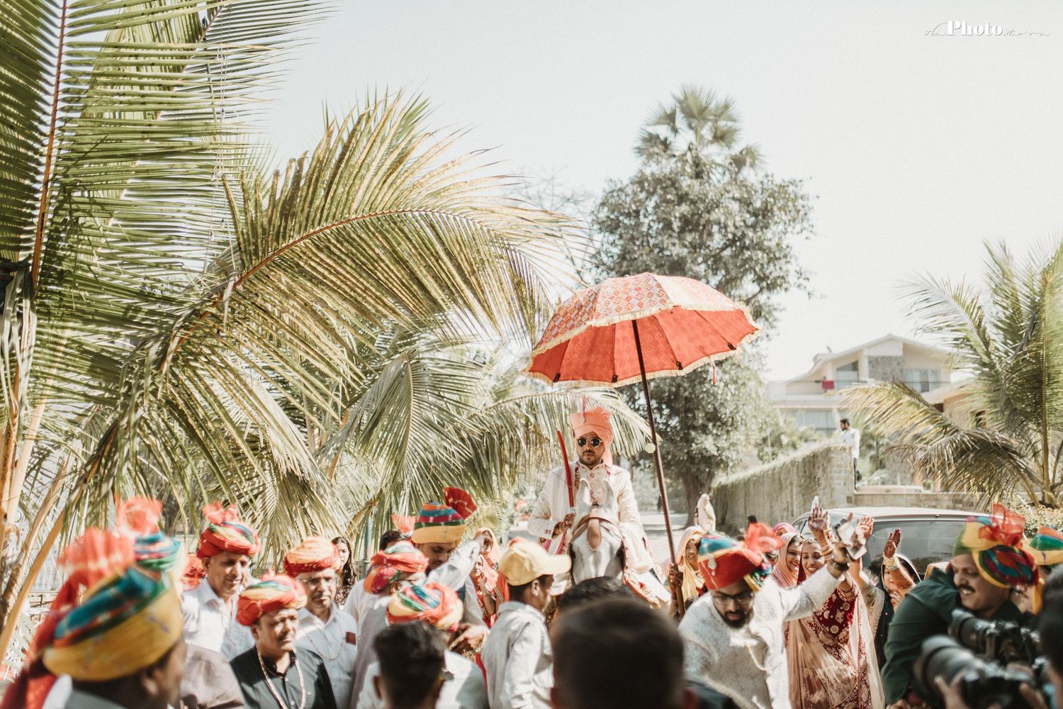 Outdoor Indian wedding celebration with coral umbrellas and palm trees creating a festive atmosphere.