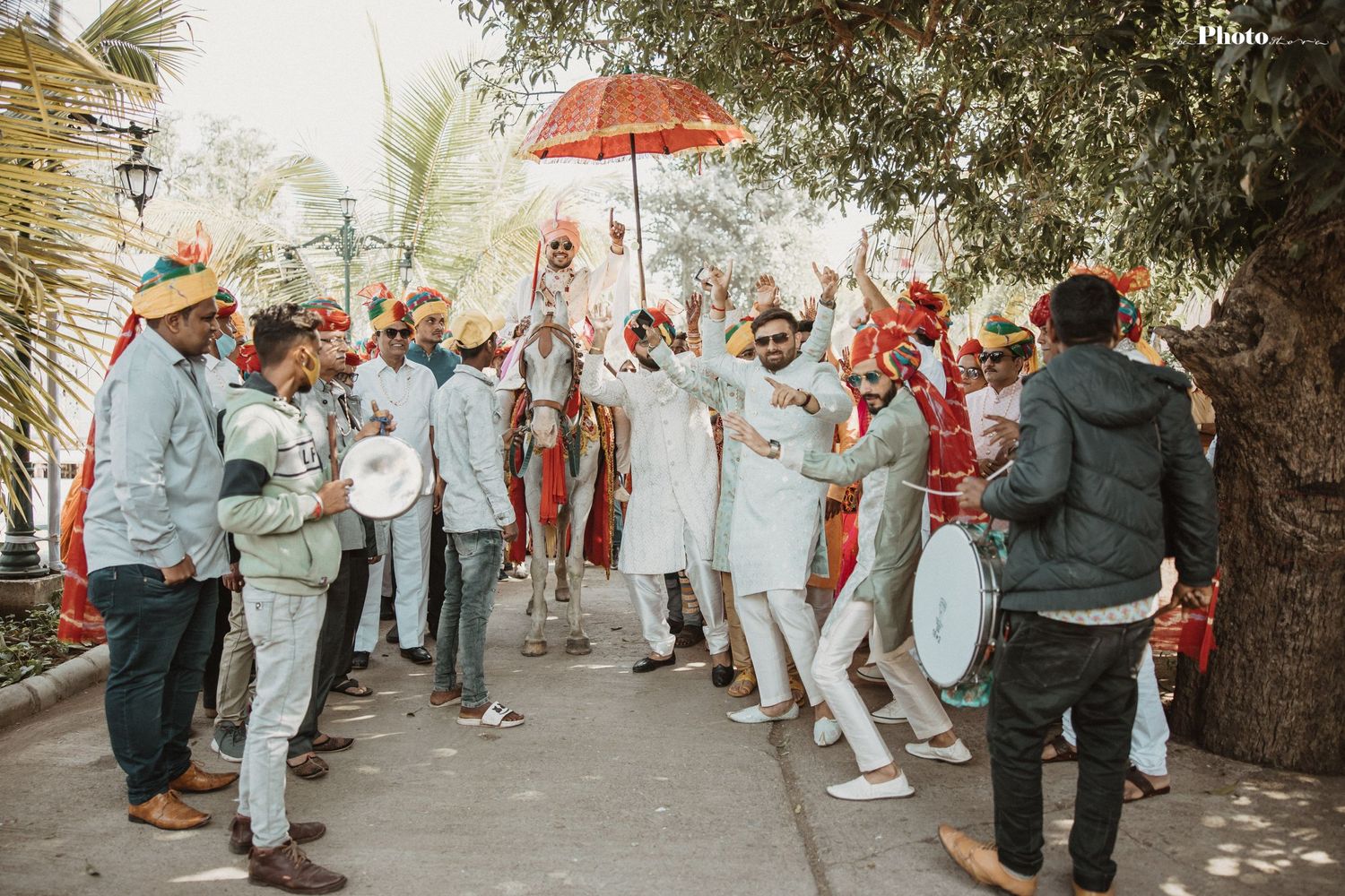 Wedding guests celebrate joyfully with a red umbrella during an outdoor ceremony.