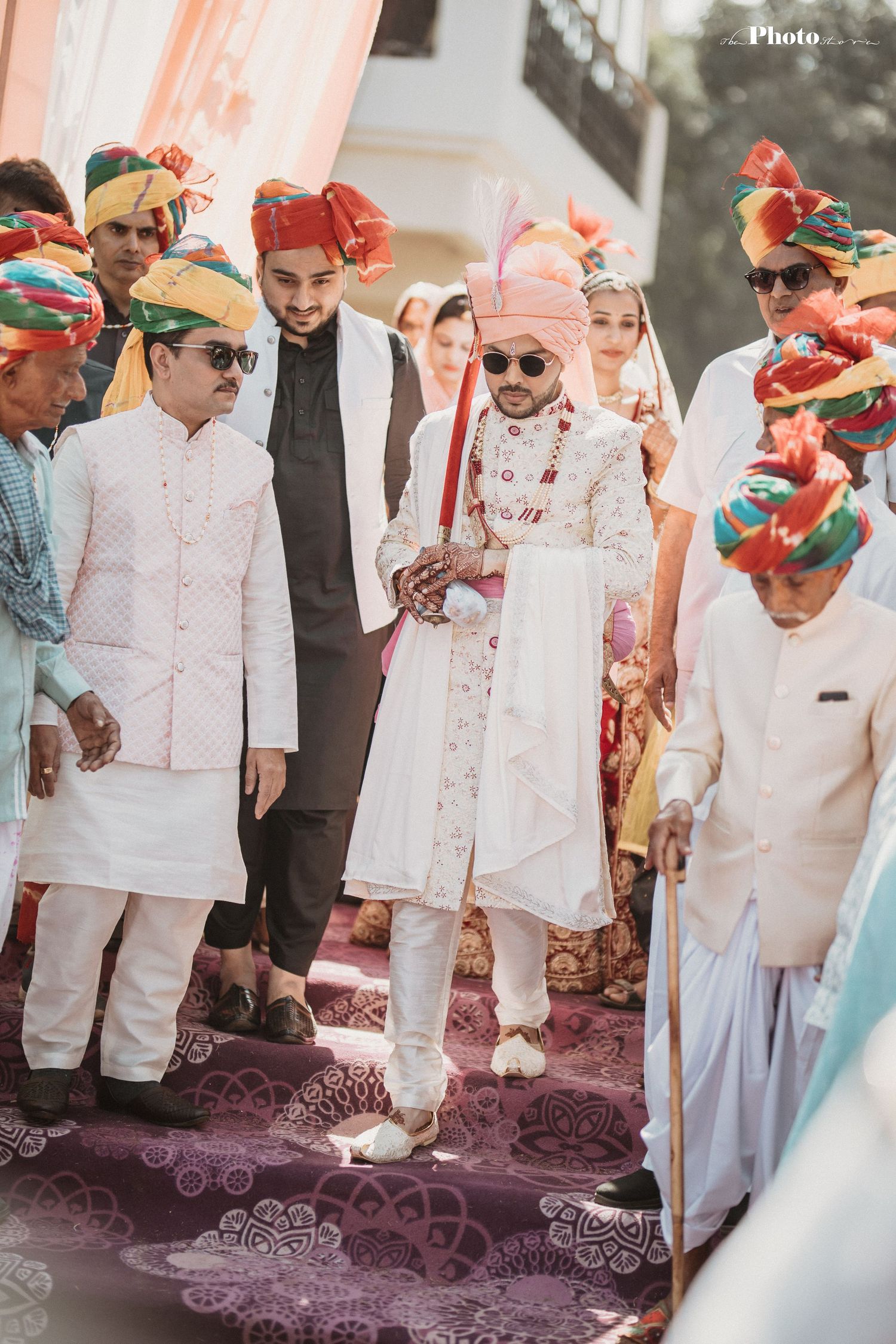 Wedding party members in white traditional attire stand on decorative carpet during ceremony.