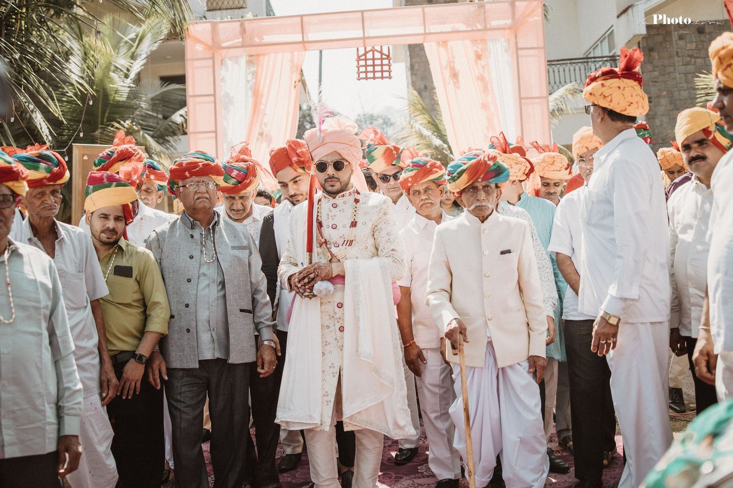 Large group in white attire poses against pink wall during traditional celebration.