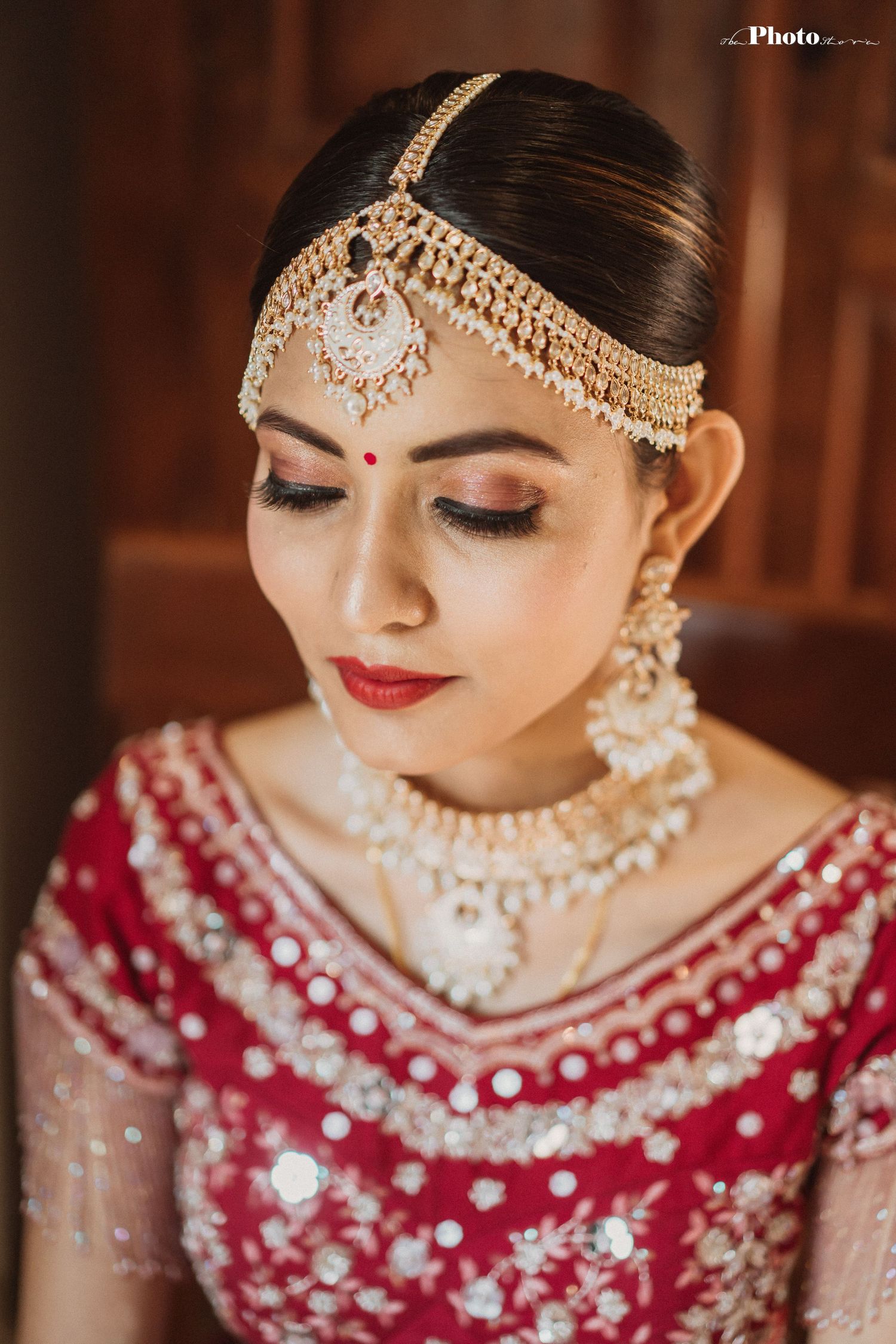 Close-up of Indian bridal makeup and jewelry featuring gold mathapatti and red lehenga.