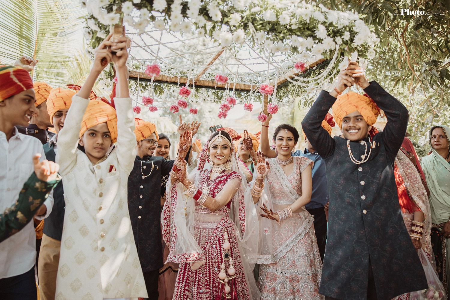 Wedding party celebrates under floral decorations with flower petals falling.