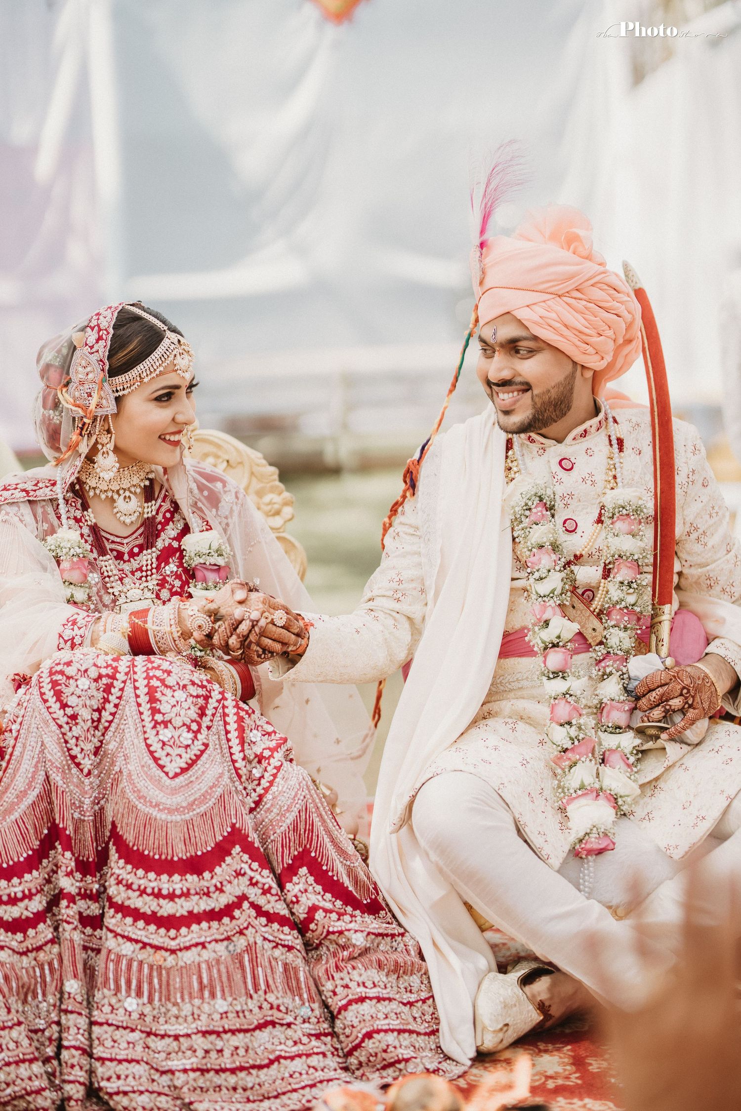 A traditional Indian wedding ceremony with the couple seated on ornate cushions during rituals.