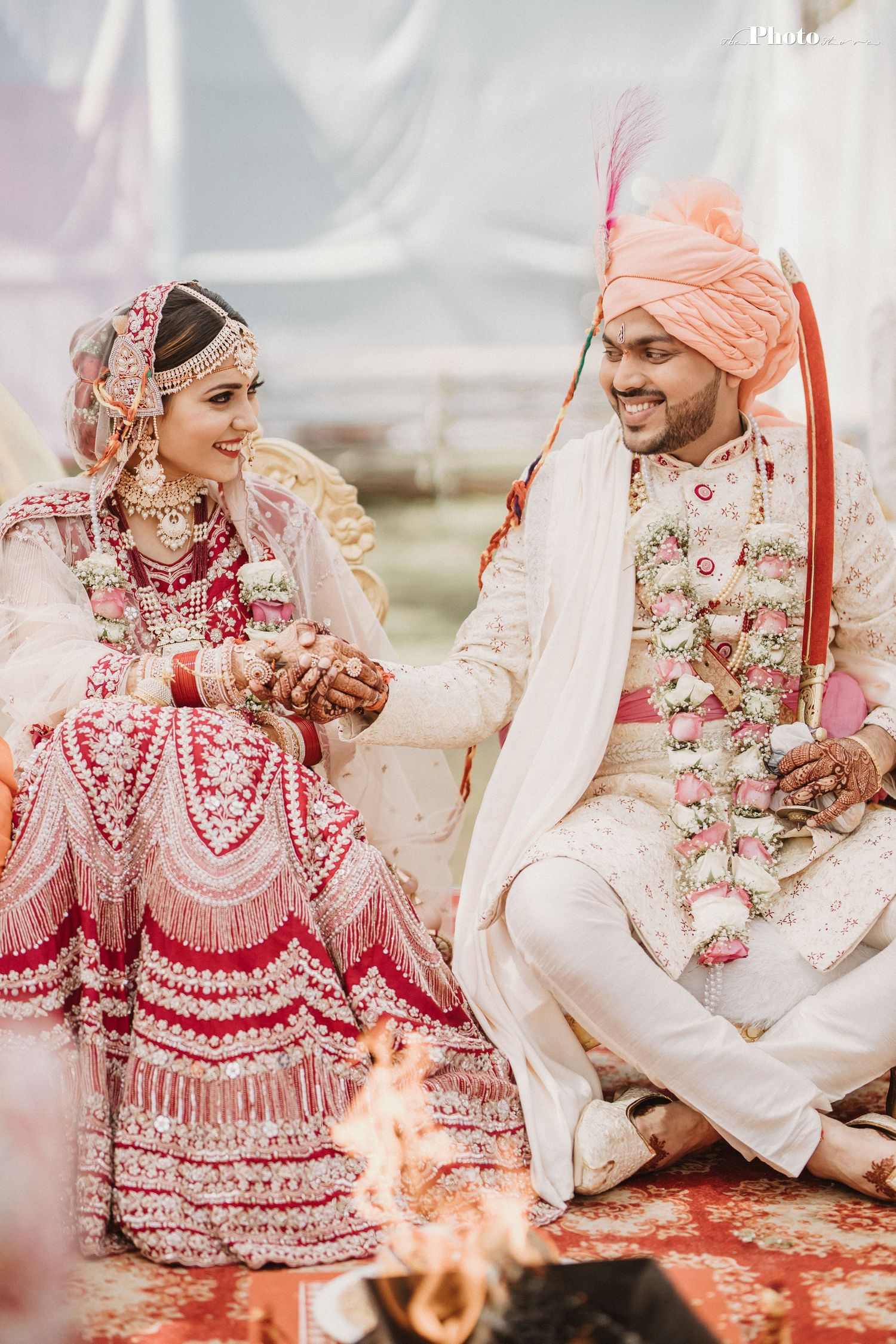 Wedding couple in traditional Indian attire performing ceremonial rituals under a white canopy.