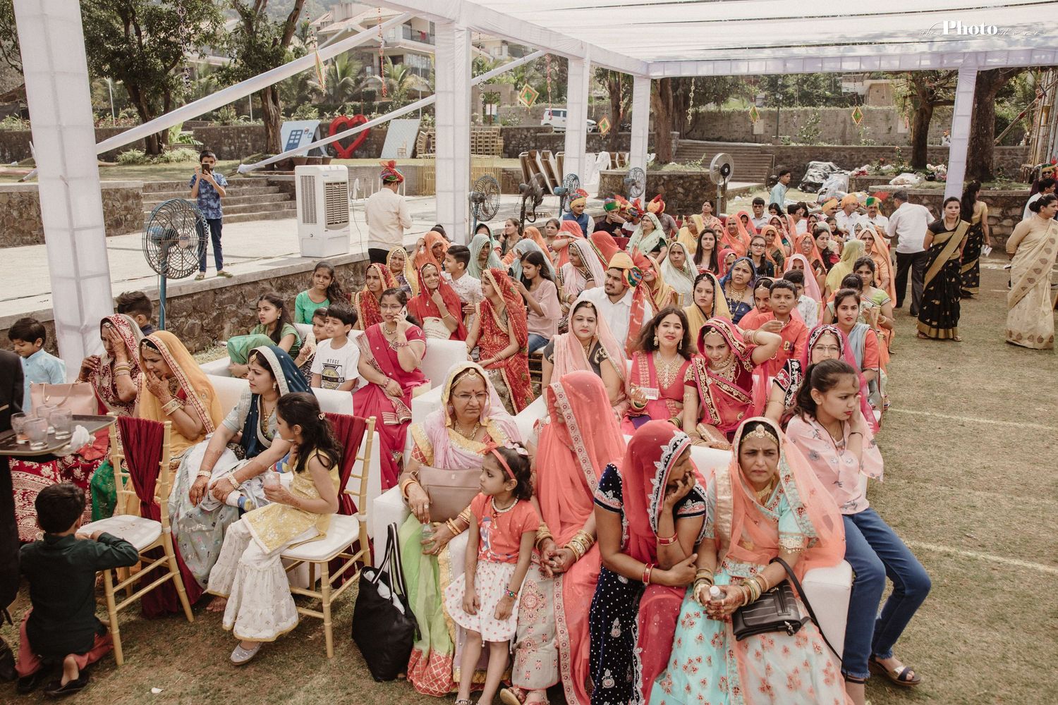 Panoramic shot of wedding guests gathered under white tent for an outdoor Indian celebration.