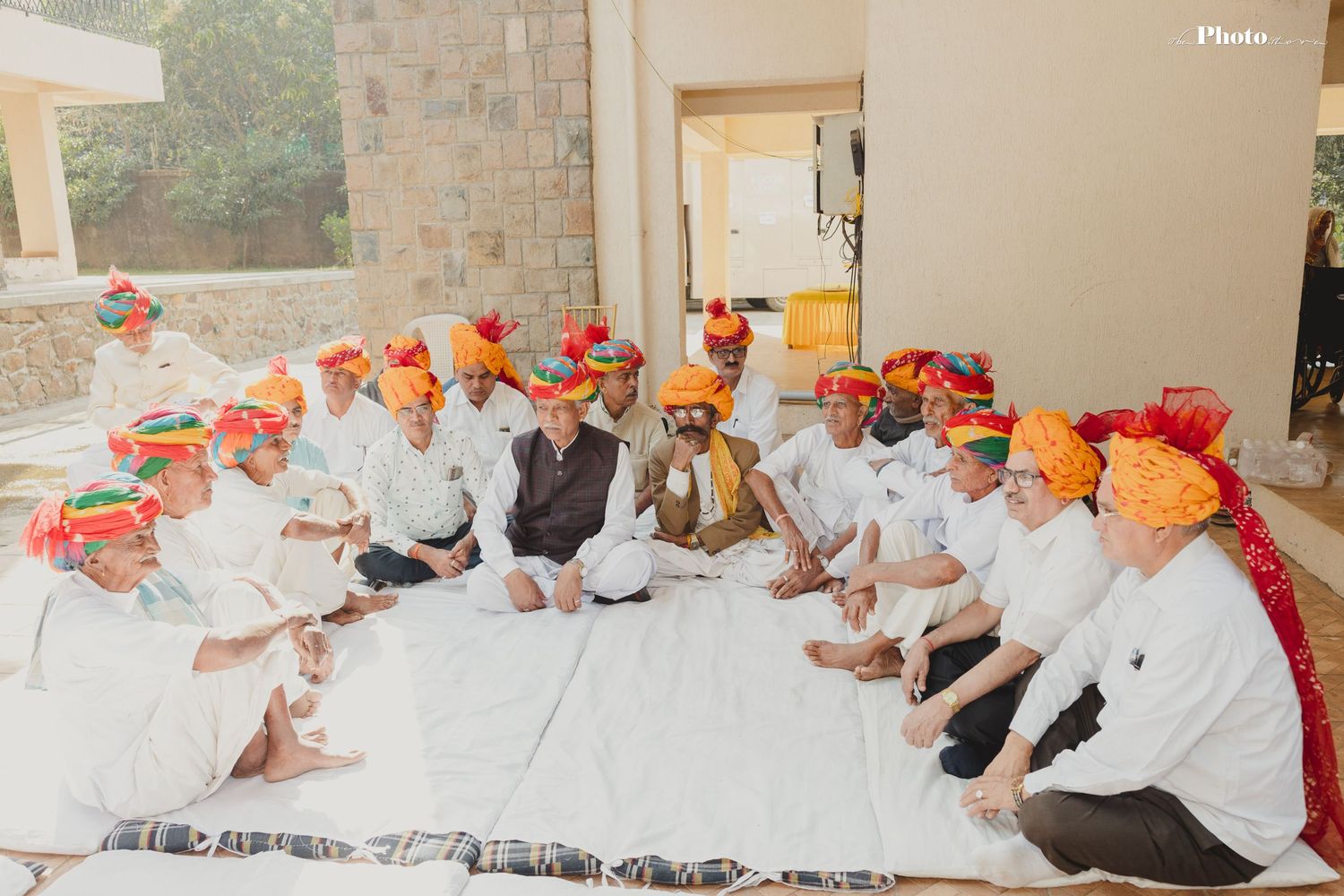 Group photo of wedding guests seated wearing traditional orange turbans at Indian ceremony.