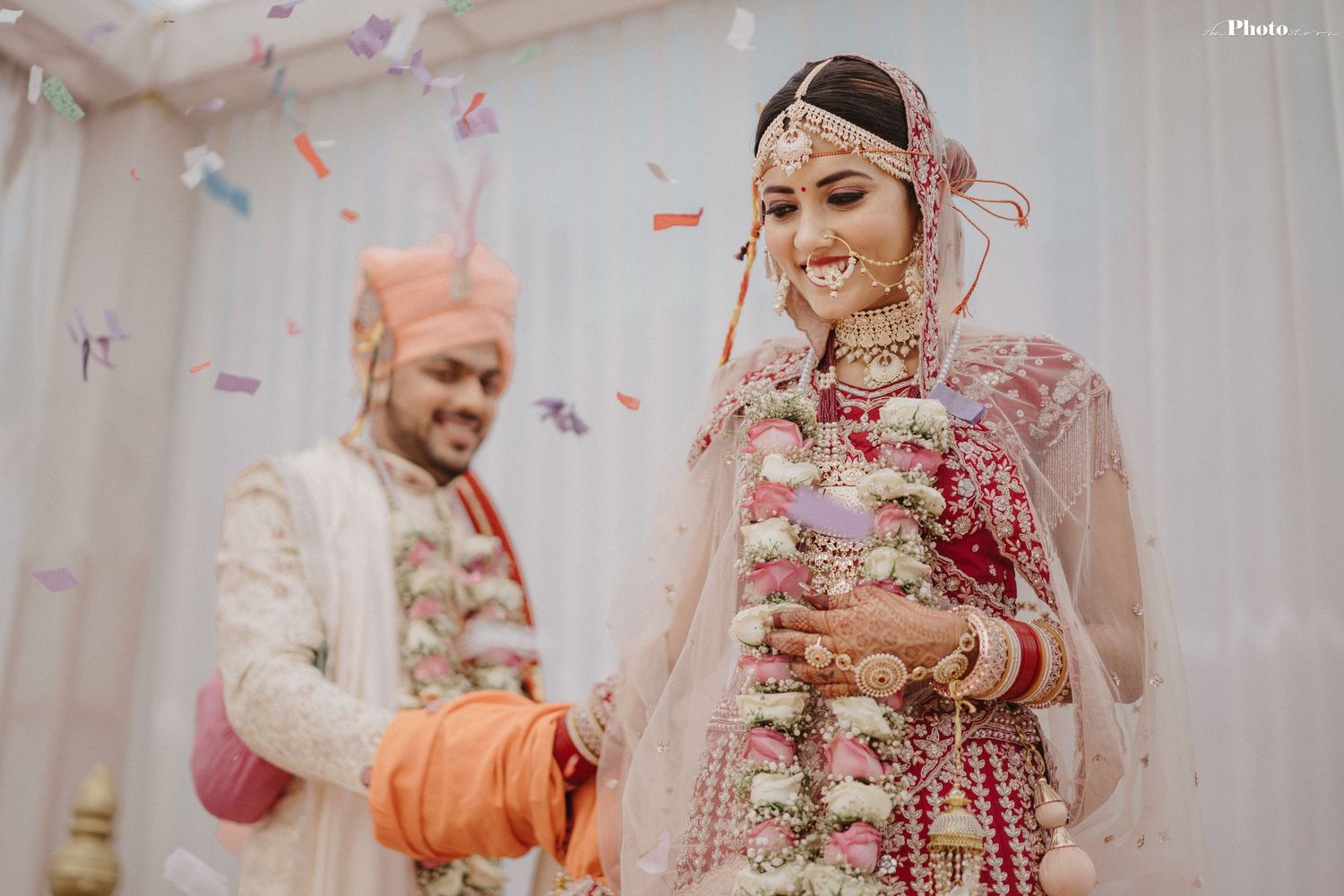 Traditional Indian wedding ceremony with bride in red lehenga and groom in cream sherwani.