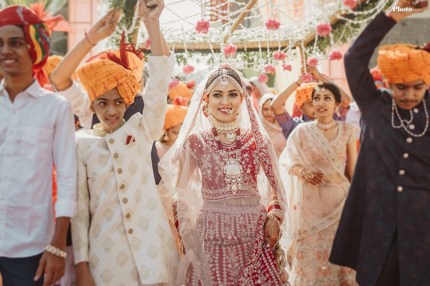 Traditional Indian wedding ceremony with vibrant red and orange attire under decorated mandap with floral arrangements.