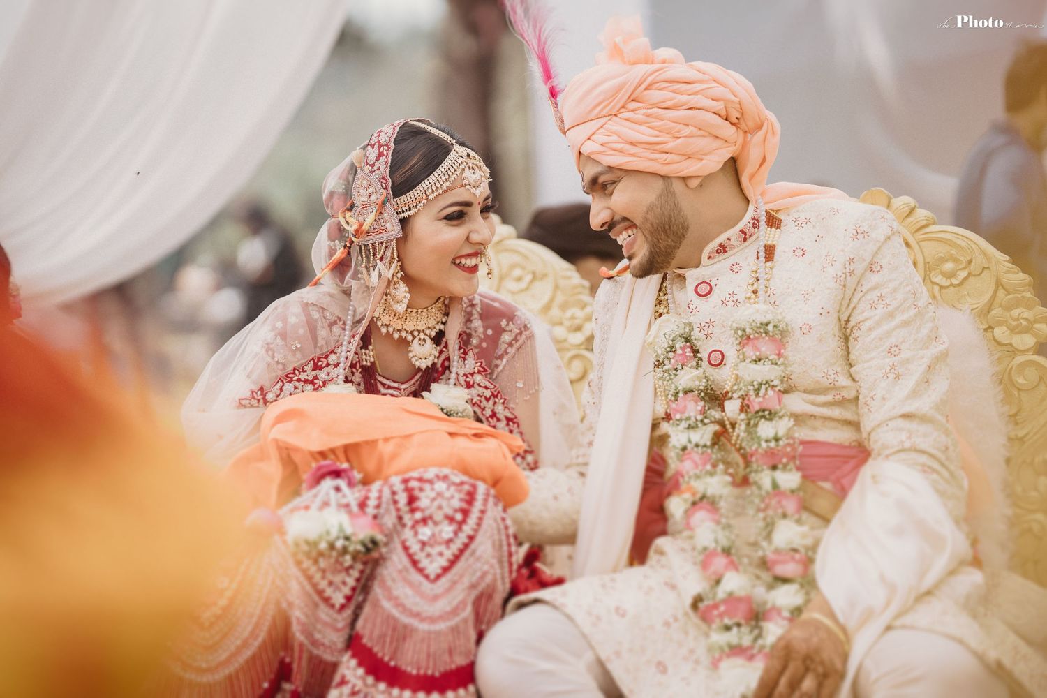 Candid moment during Indian wedding ceremony with couple in traditional red and cream attire.
