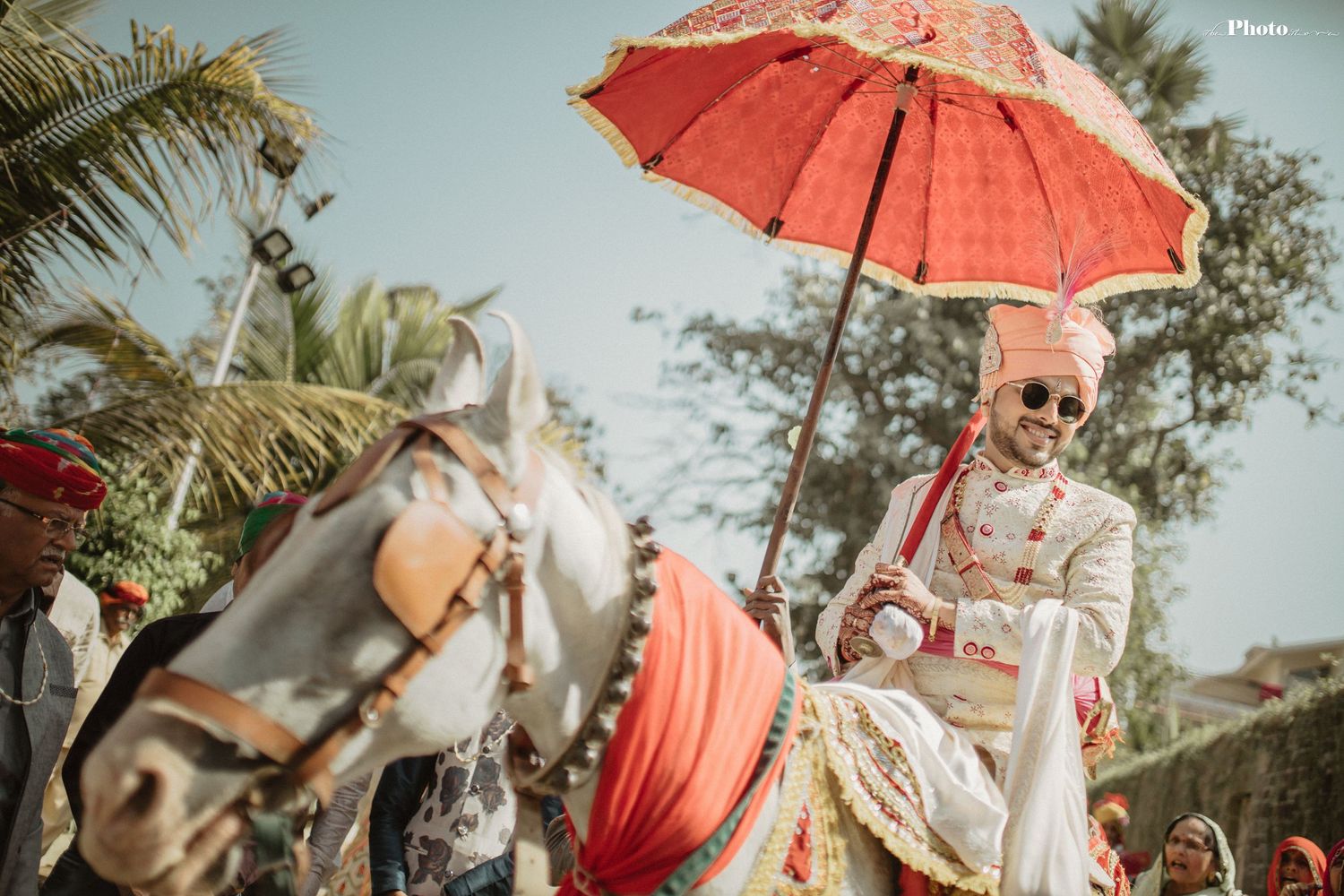 Outdoor Indian wedding ceremony with decorative red umbrellas and natural scenery.
