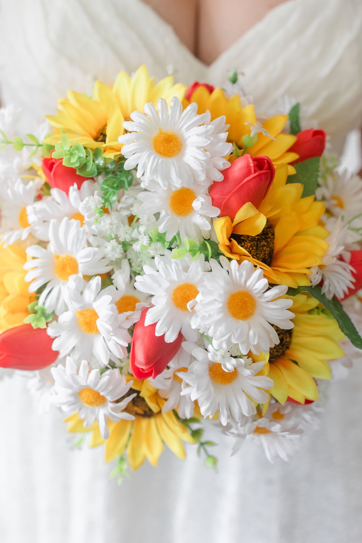Colorful bridal bouquet with sunflowers, daisies and coral flowers against white dress.