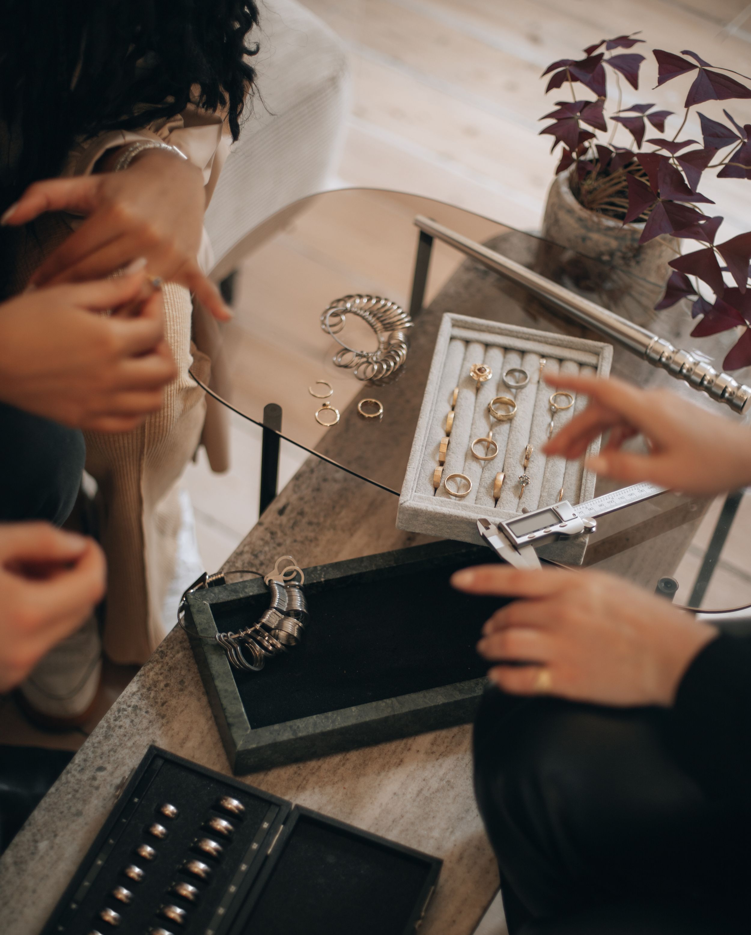 Hands arranging jewelry and rings on textured surface in moody lighting.