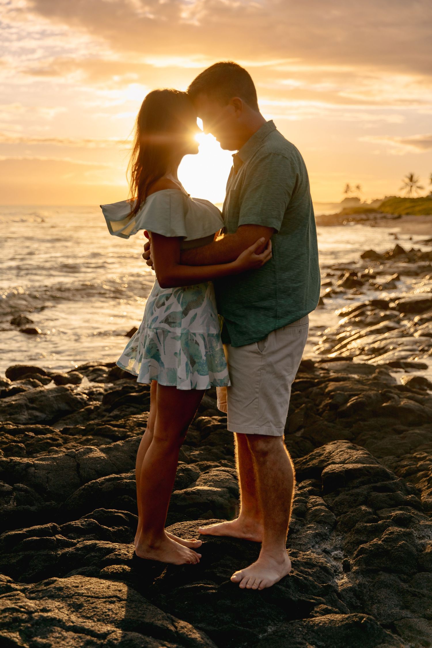 Romantic couple embracing on rocky shore during golden sunset.