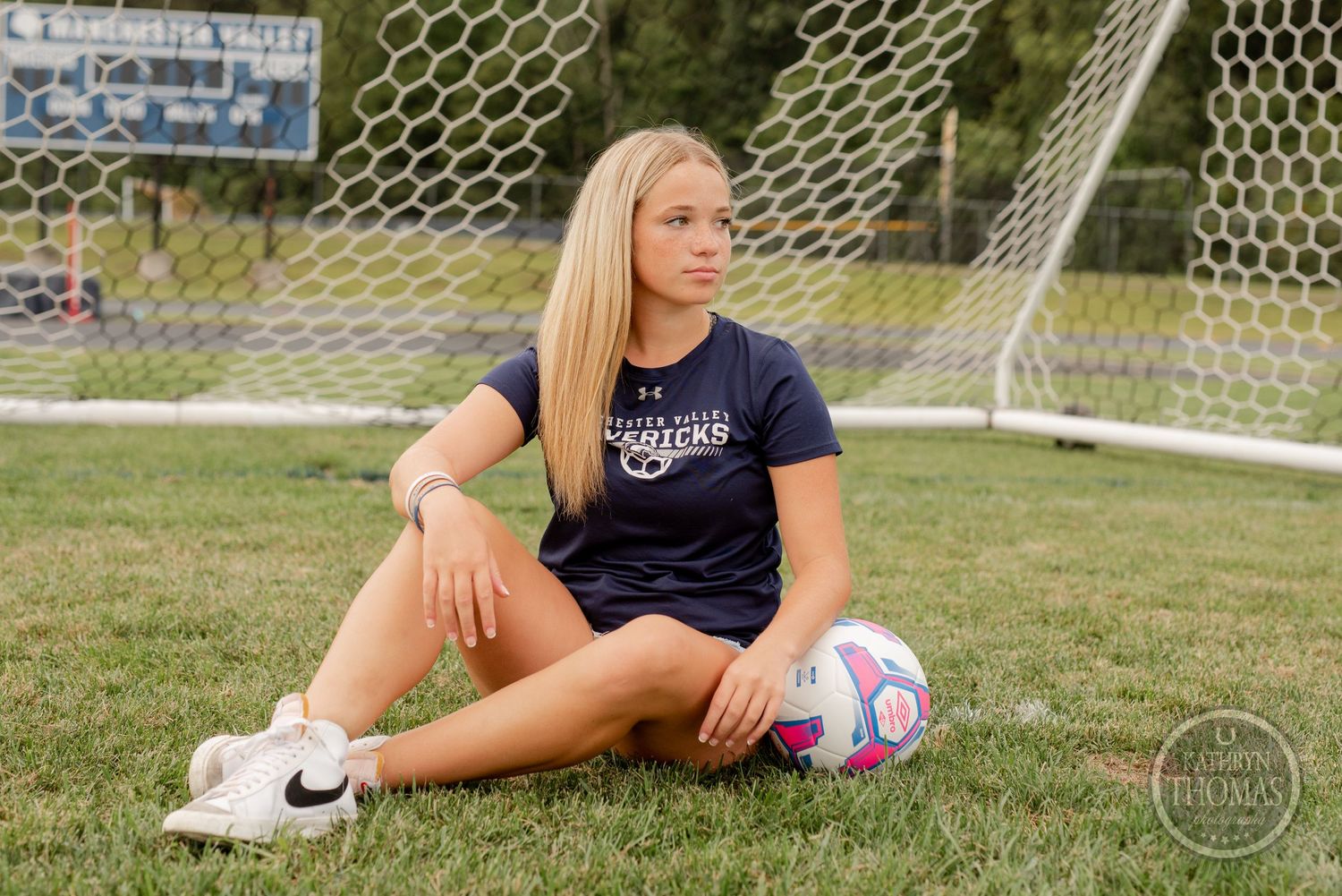 Soccer player relaxing on field with colorful ball near goal net.