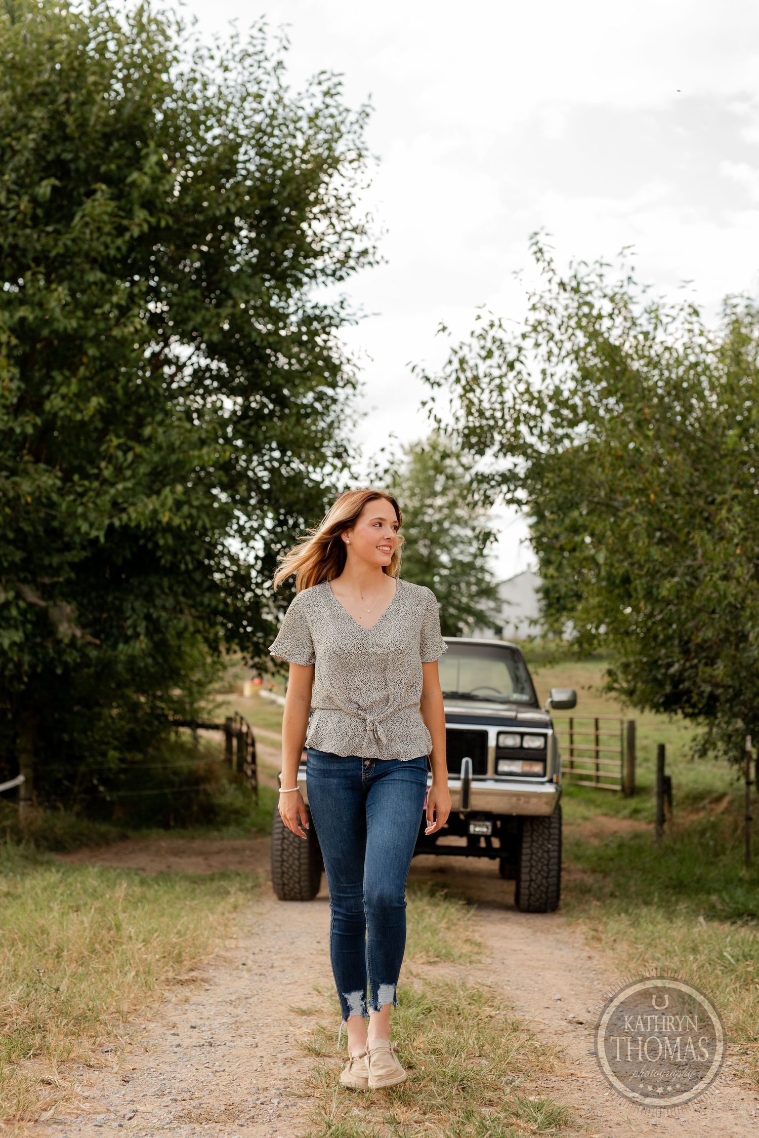 A person walks down a dirt path with a vintage Land Rover visible in the background.