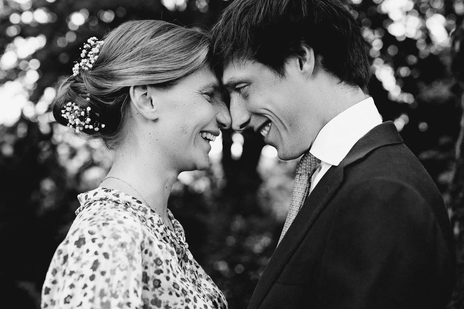 Black and white close-up of a romantic couple touching foreheads and smiling.