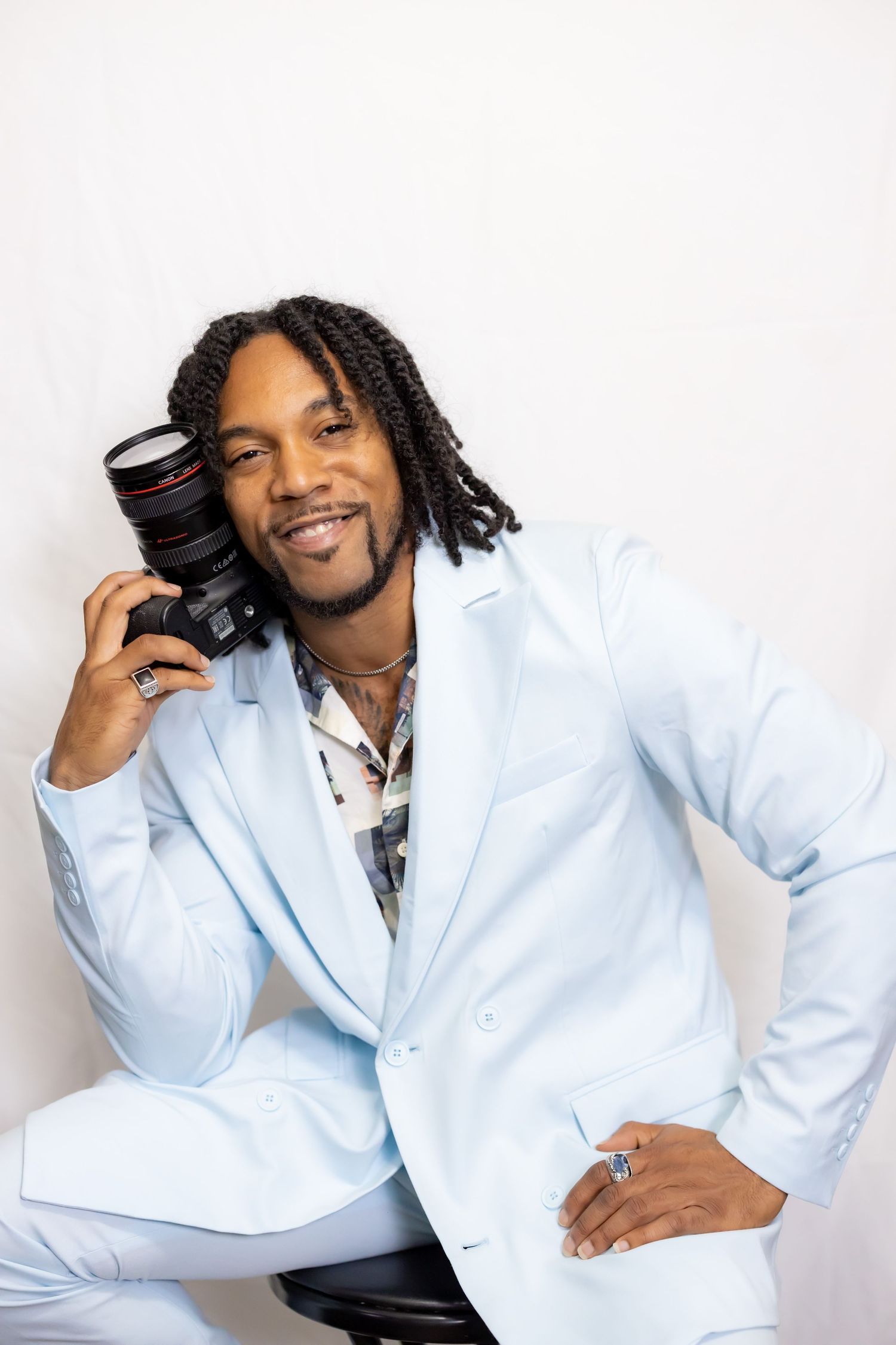 Professional photographer in light blue suit posing with camera against white background.