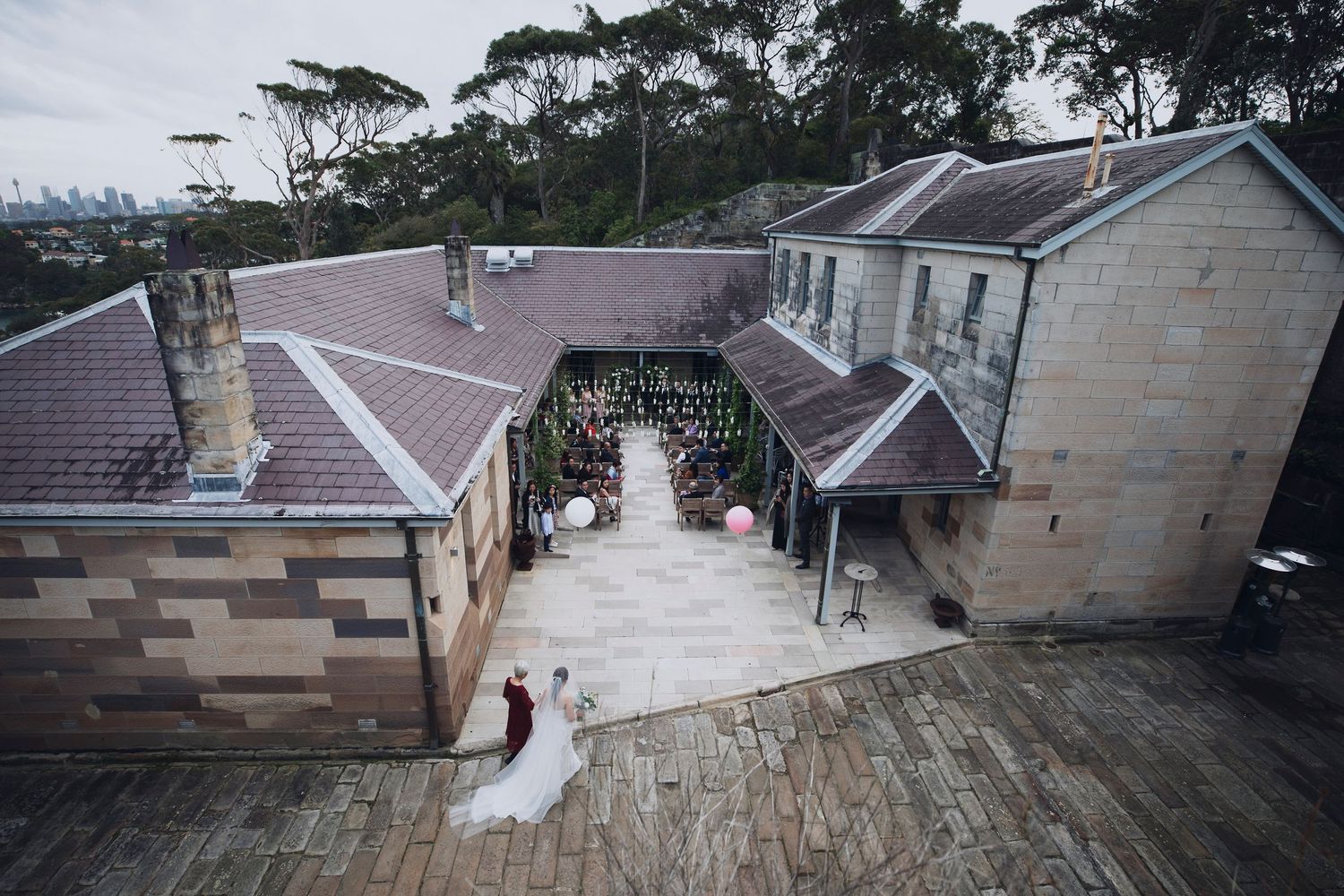 Aerial view of wedding couple at historic sandstone venue with guests in courtyard.