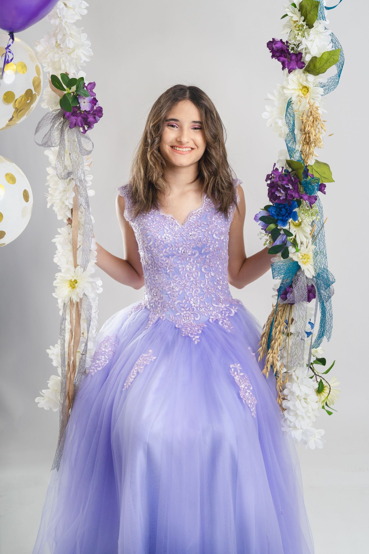 Quinceanera portrait with purple ball gown and floral balloon arch decorations.
