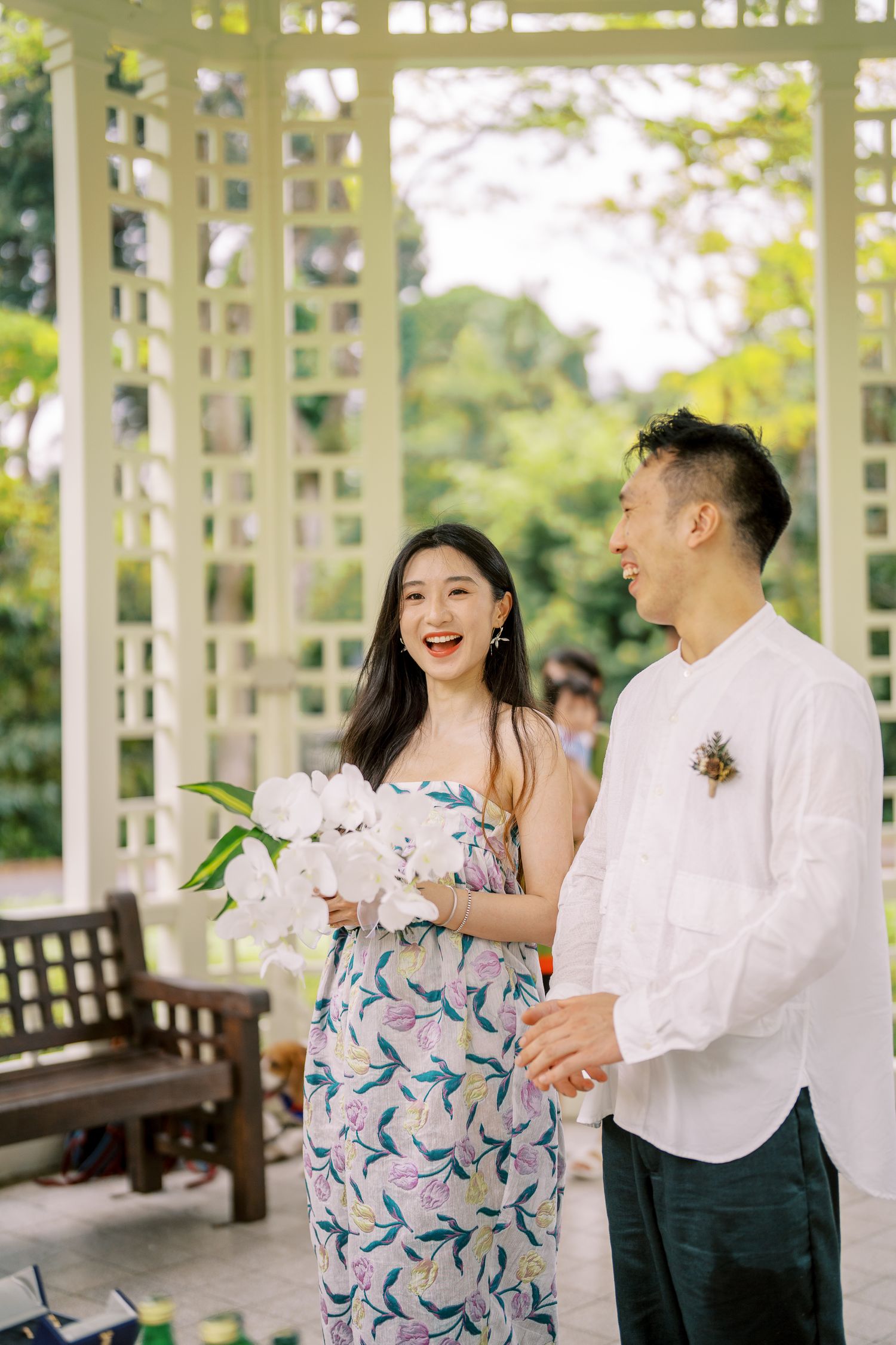 A couple shares a joyful moment in a white garden pavilion with floral decorations.